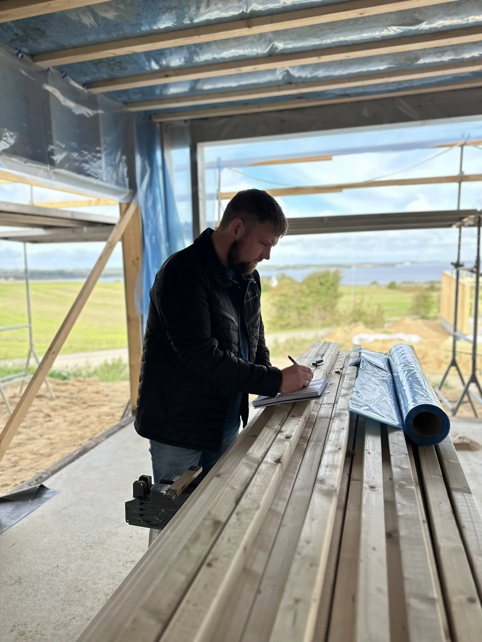 Martin Holm noterer mål ved tømmeret i et nyt råhus med udsigt over Limfjorden